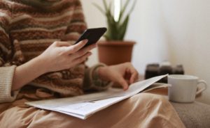 Woman holds newspaper in one hand and phone in the other