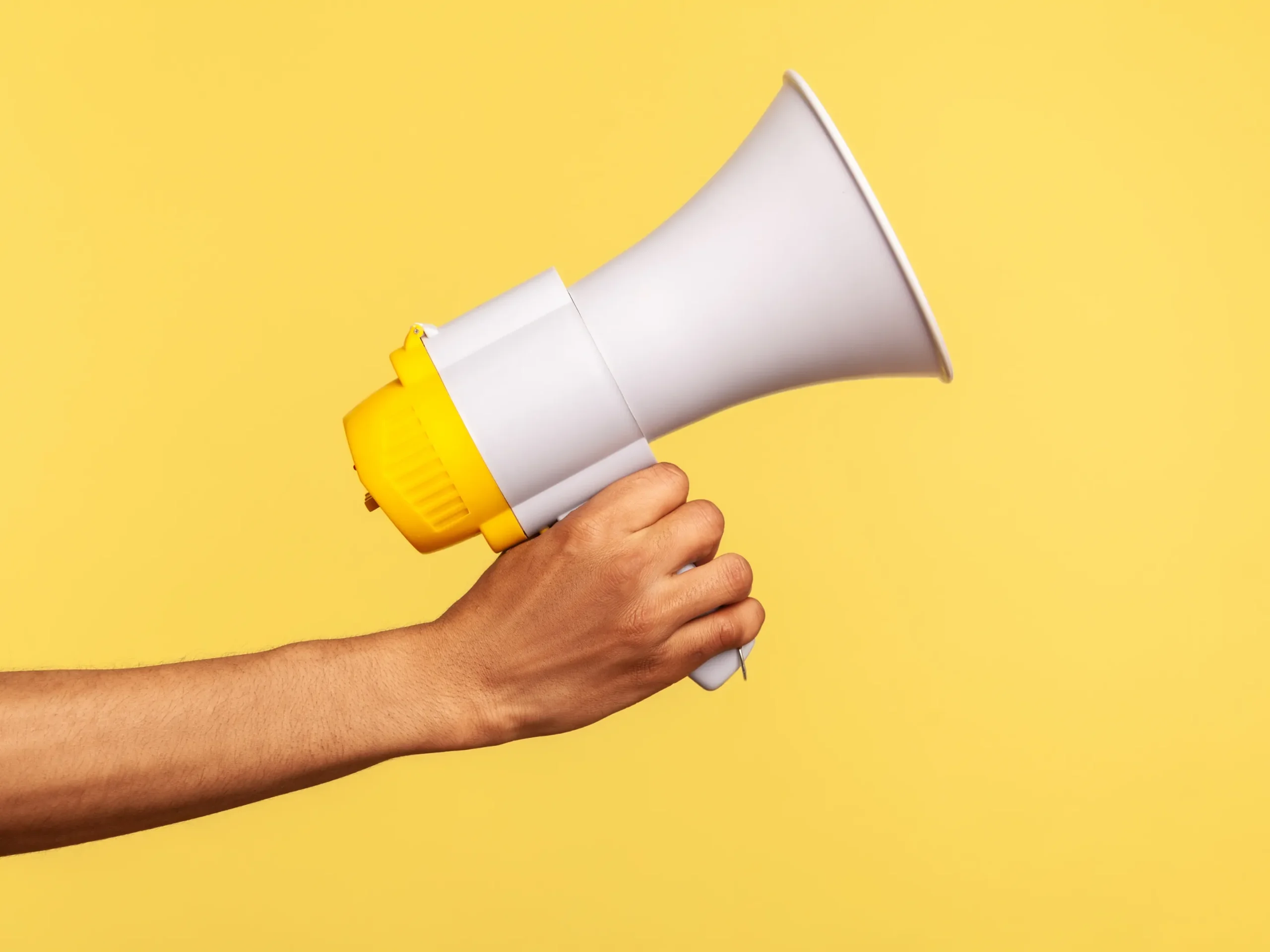 hand holding a megaphone in front of a yellow background: representing starting repetition in advertising